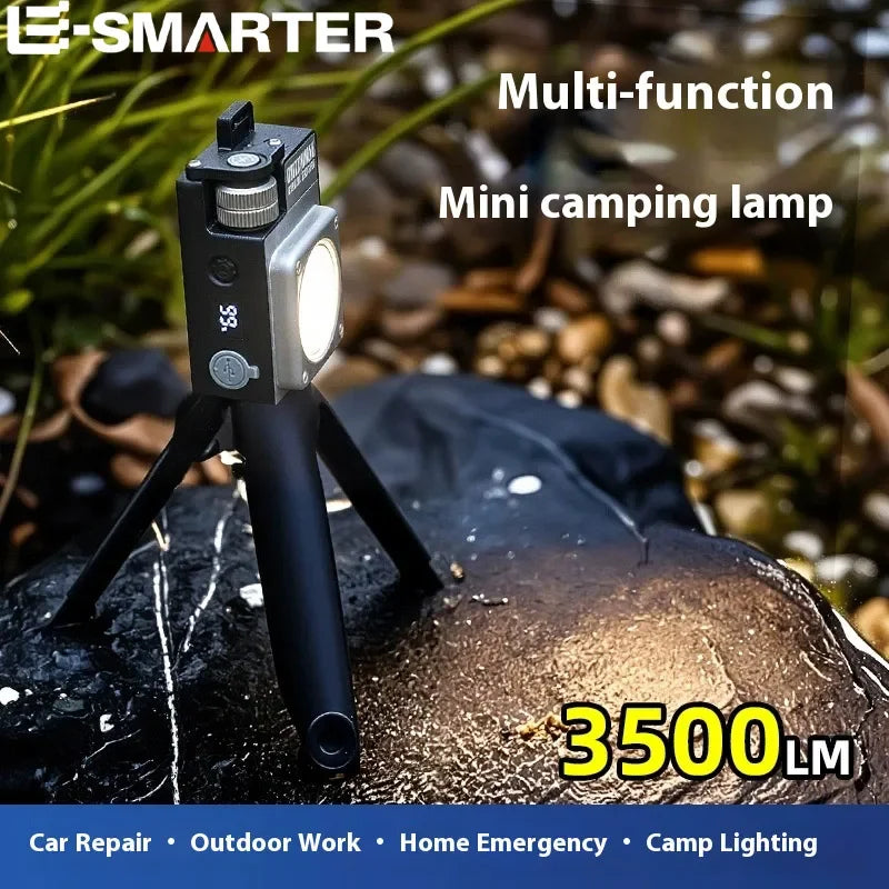 A compact black and silver mini camping lamp on a small tripod, shown outdoors on a wet rock with blurred natural background. Text overlays read 'E-SMARTER', 'Multi-function Mini camping lamp', and '3500LM'.
