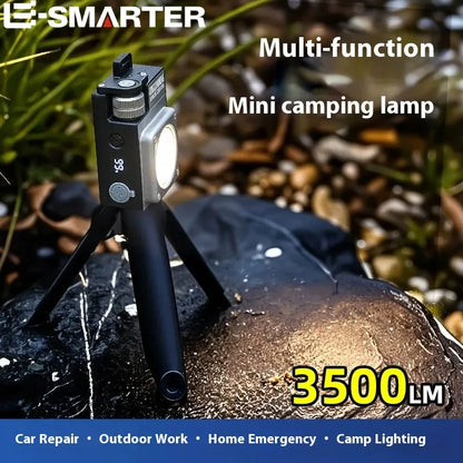 A compact black and silver mini camping lamp on a small tripod, shown outdoors on a wet rock with blurred natural background. Text overlays read 'E-SMARTER', 'Multi-function Mini camping lamp', and '3500LM'.